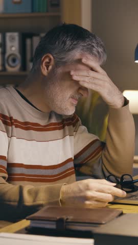 Tired stressed man working late at night on his laptop, He is suffering from headache and eye strain