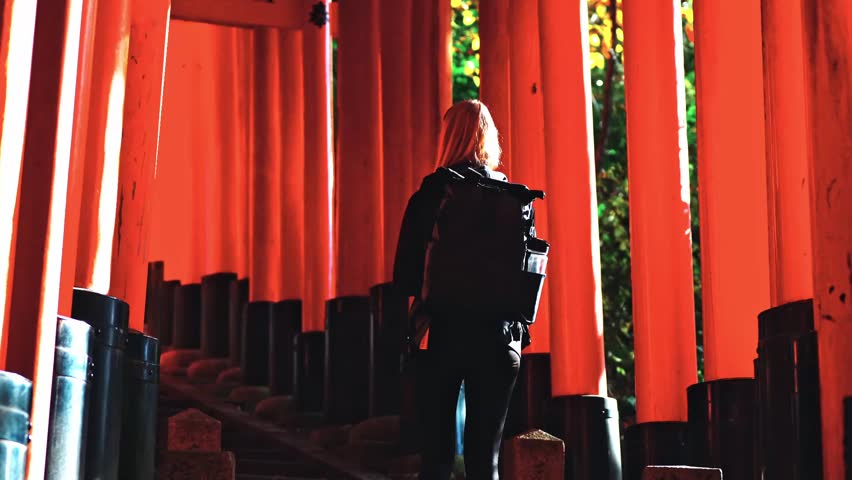 A woman ascends the stone steps of Fushimi Inari Shrine in Kyoto, Japan, surrounded by rows of vibrant vermilion torii gates.