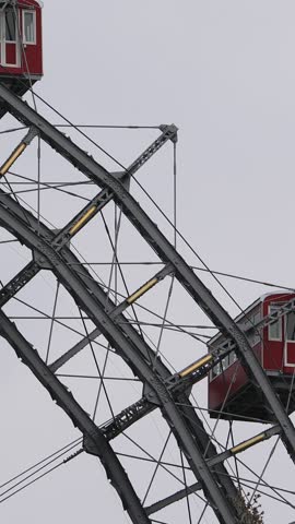 A detailed view of the Vienna Ferris Wheel in Prater park with its iconic red gondolas and steel frame under a cloudy sky. Built in 1897 as a historic landmark
