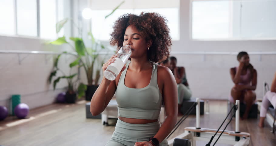 Woman, drinking water and pilates break at gym, sports drink and hydration for wellness at club. Workout, person and aqua beverage for liquid nutrition, rest and thirsty recovery with electrolytes