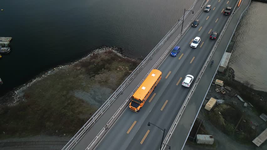 Aerial View Of A Yellow School Bus Driving Across A Bridge Connecting Halifax To Dartmouth, Nova Scotia. The Sunny Summer Day Provides A Beautiful Backdrop To The Journey Across The Water.