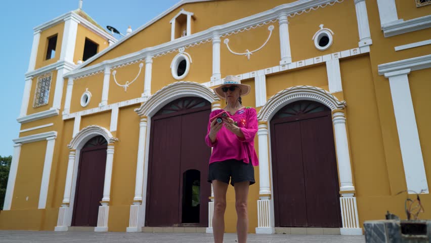 A smiling mature woman captures a joyful selfie in front of a historic church in Moyogalpa, Ometepe Island, Nicaragua, embracing their travel adventure.