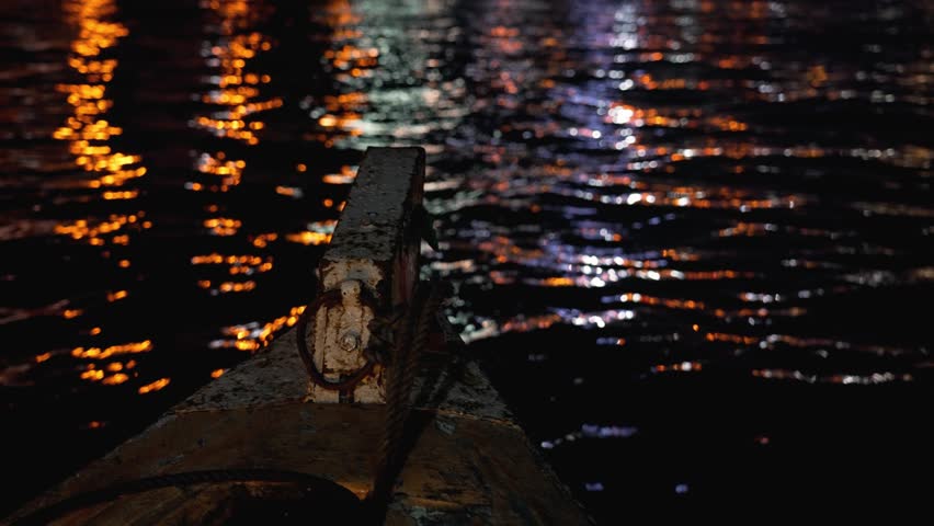 Canoe on urban canal. Old wooden boat gliding through the water on a river in night time. Аn old rusty boat is sailing across the water. 