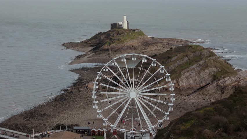 The Big Wheel rotating with a Mumbles Lighthouse at background in Mumbles Pier Swansea of England. Aerial view.