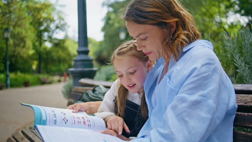 Closeup family learning at park. Attentive woman parent staring school copybook doing homework with small child at bright greenery place. Mother daughter sitting bench studying together at fresh air - Powered by Shutterstock - Get 15% off with code: PIKWIZARD15