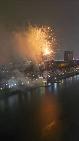 A stunning fireworks display over a river at night, with colorful reflections on the water and a city skyline in the background. A vibrant celebration scene.
