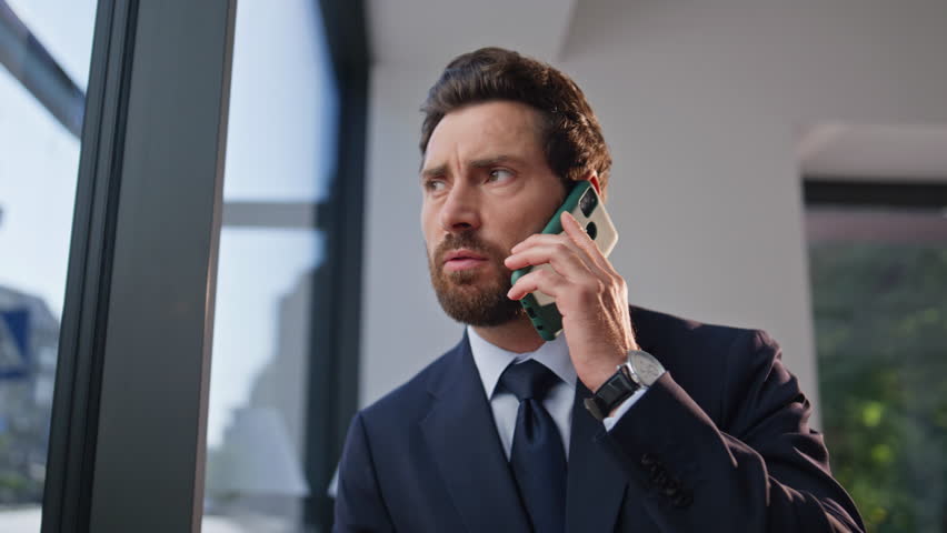 Worried ceo talking mobile phone sitting cozy cafeteria table alone zoom out. Serious businessman discussing work in cellphone call at coffee break. Concerned cafe visitor in suit speaking emotionally