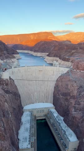 Monumental Hoover Dam silhouetted against Lake Mead, nestled in rugged Nevada landscape, glowing under warm sunset light with majestic mountain backdrop
