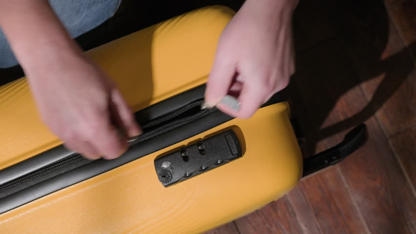 Woman hands closing zipper on yellow travel suitcase in room close-up top view. Concept of packing luggage for journey.