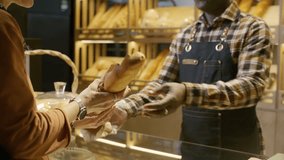 Baker in apron handing fresh baguette to female customer in cozy bakery with wooden shelves filled with fresh bread in background. Close-up shot - Powered by Shutterstock - Get 15% off with code: PIKWIZARD15