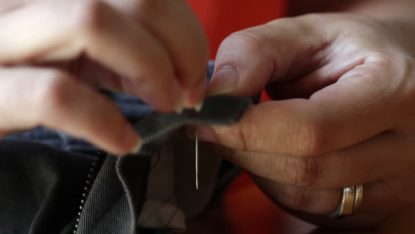 Detail of hands sewing a button on to a pair of shorts.