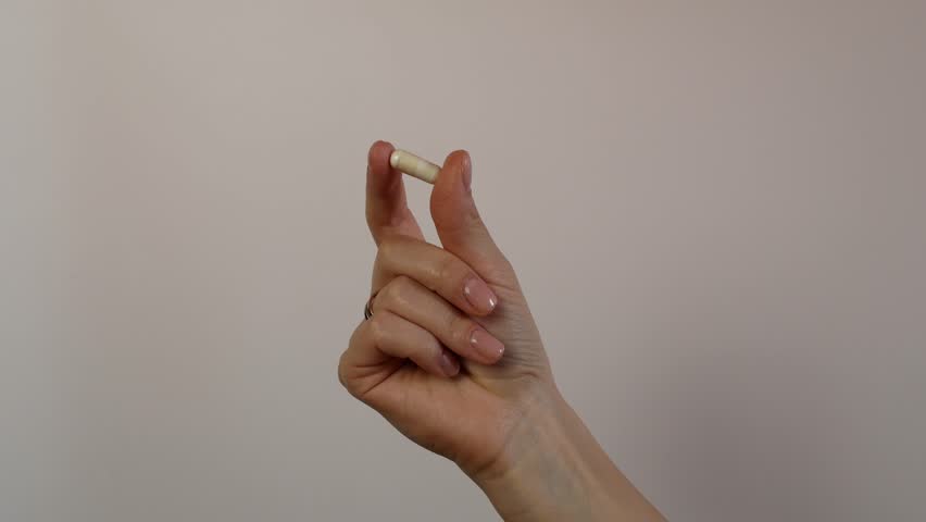 A girl holds a white pill in her fingers, shot in close-up. A woman takes her medicine every day. Taking care of her health. Vitamins to maintain immunity.