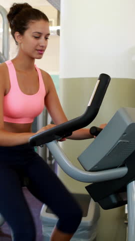 Vertical Video of fit brunette working out on the exercise bike at the gym