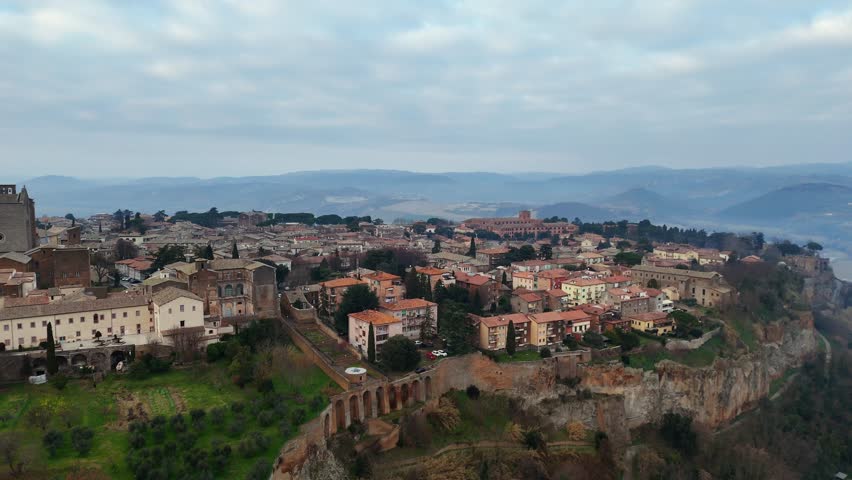 Aerial view of Orvieto, a charming Italian city built on a tufa cliff, surrounded by green hills and overlooked by a cloudy sky