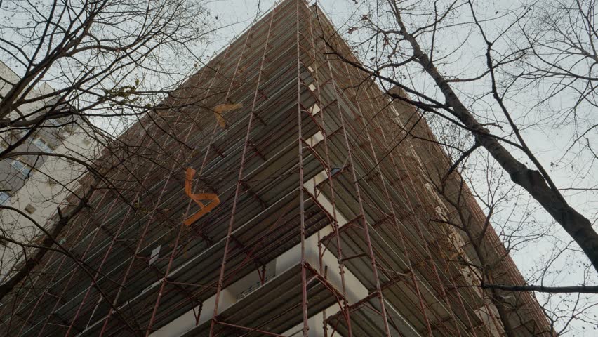 Construction workers are installing scaffolding on an apartment building to prepare for block insulation. This project focuses on enhancing thermal efficiency and rehabilitation.