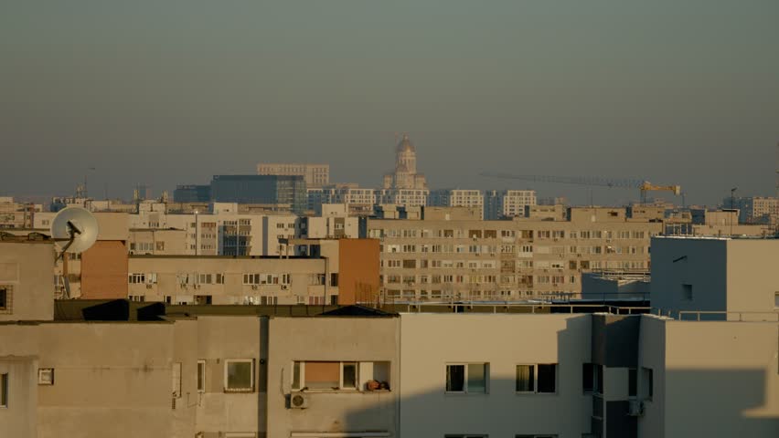 Observe the skyline of Bucharest with residential apartment blocks and the prominent National Salvation Cathedral in the background during golden hour.