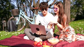 Young couple reclining on colorful blanket during sunny park day, sharing laptop moment with relaxed connection and casual enjoyment of outdoor leisure time - Powered by Shutterstock - Get 15% off with code: PIKWIZARD15