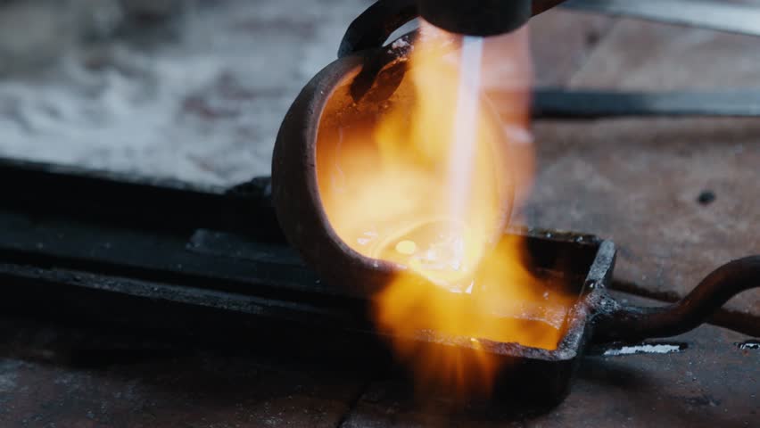 Jeweler pouring molten gold into ingot mold and heating it