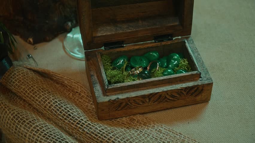 Gold rings lie among pebbles in a wooden fairy-tale box. Presentation of jewelry in a craft box.