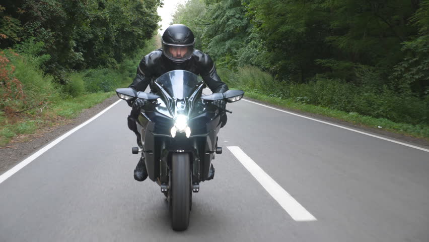 Young man in helmet riding on modern sport motorbike at rural forest road. Motorcyclist racing his motorcycle on wood route. Guy driving bike during trip. Concept of freedom and adventure. Front view