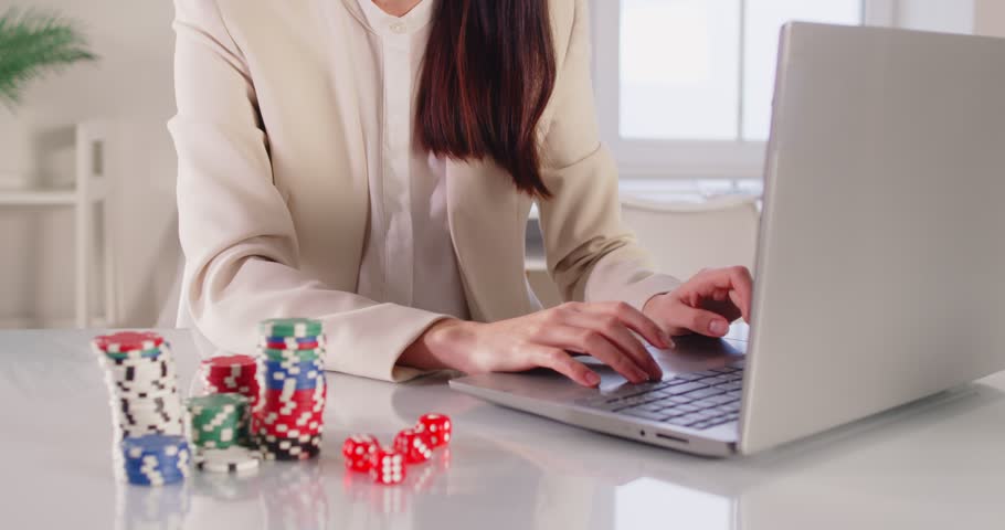 Faceless businesswoman happy about victory in online casino, sitting in front of laptop and clenching fists as sign of success, gabbing pocker chips, plays in roulette, being addicted 