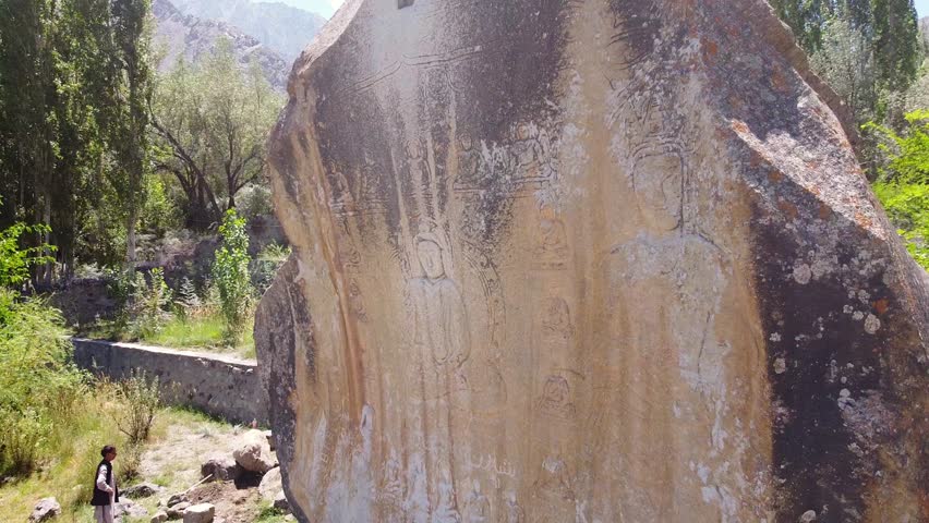 Pull back drone shot of Skardu Manthal picturesque view of Carved Buddha large granite rock relic on a sunny blue sky day in pakistan.