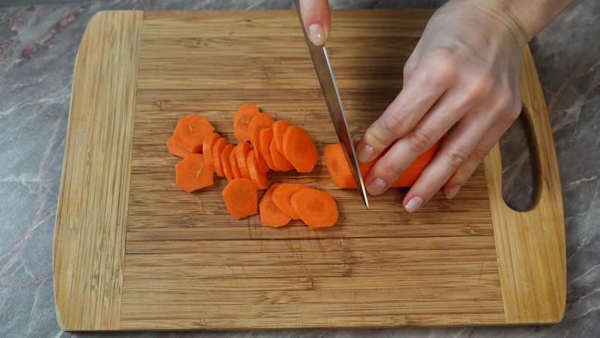 A woman is cutting carrots on a wooden cutting board. Home vegetable preparation. Close-up.