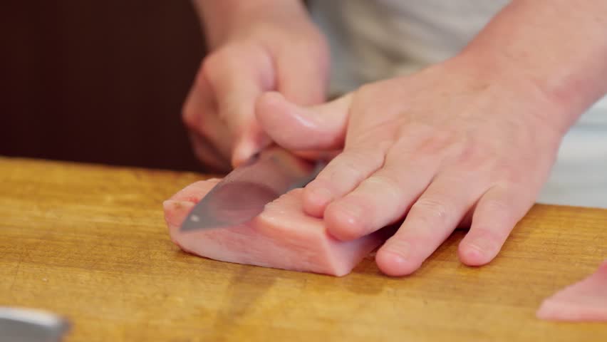 The hands of a sushi chef cutting fatty tuna