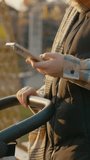 Vertical Screen: Multitasking mother gently rocking baby stroller while browsing smartphone during golden sunset in urban park landscape - Powered by Shutterstock - Get 15% off with code: PIKWIZARD15