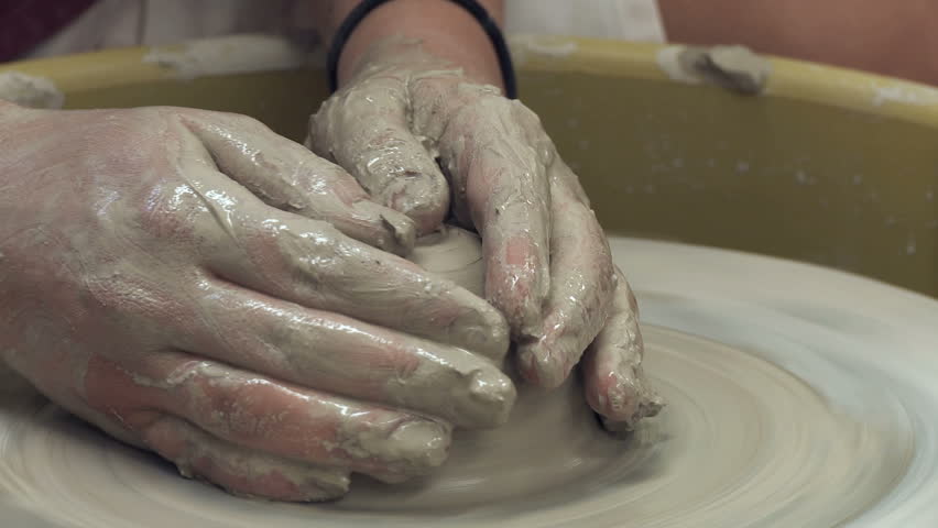 Craftsperson's hands shape a pot out of wet clay using a potters' wheel.