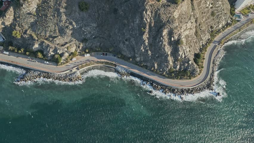 A stunning aerial top-down view of the Almunecar Coast in Spain. This drone footage captures the winding coastal road along the rocky shoreline