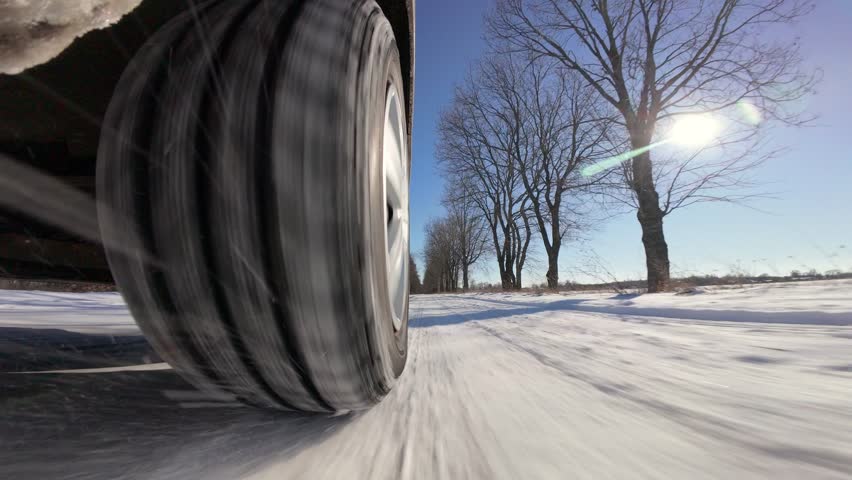 Car driving on snowy road in countryside. Low angle camera view of car wheel driving on road after snowfall on winter sunny day