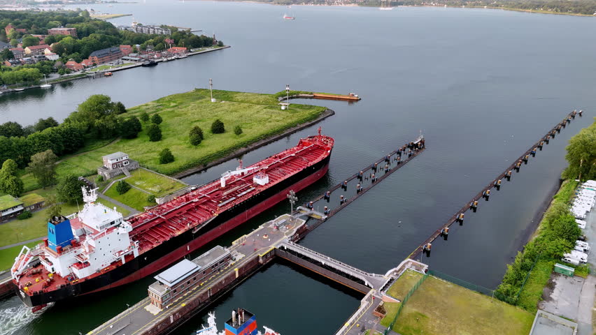 Kiel Canal Locks: Overcast Summer Day with Tanker Ship Passing Through - Green Shoreline, Grey Water, Red and Black Hull, High Angle Drone Shot, Close Up Perspective