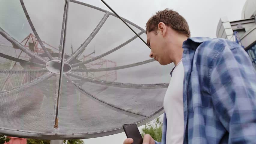 A specialist in radio telescope and dish repair diagnoses a malfunction using tests on a smartphone for troubleshooting.