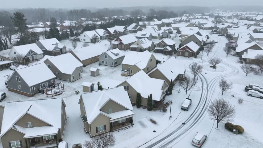 Modern american houses snow-covered after snowstorm. Rising drone wide shot. Cloudy cold and icy winter day in quiet american suburb neighborhood. New developed area in Virginia,America.