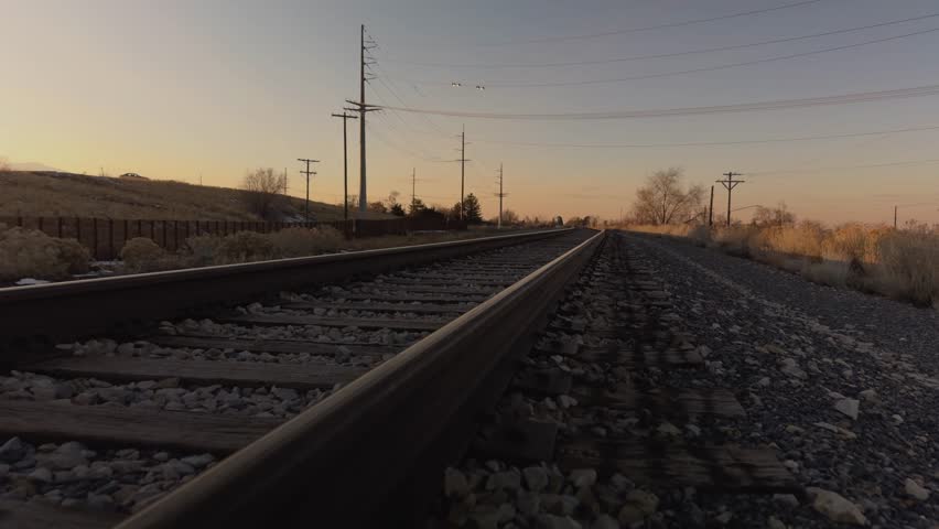 Slowly walking forward along railroad tracks at sunset, capturing shifting perspective, warm light, and distant birds in flight.