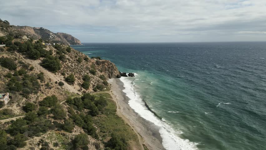 Aerial establishing of Almunecar coastline in Spain, green water waves crashing against the rocky shore, dolly