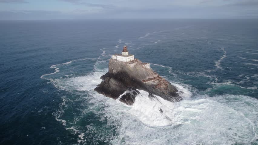 A lighthouse stands on a rocky island surrounded by the vast ocean, with waves crashing nearby