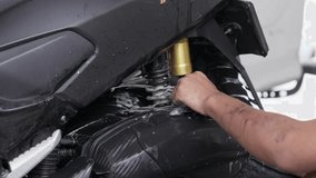 Person cleaning a motorcycle with a cloth, close-up of a shiny black frame - Powered by Shutterstock - Get 15% off with code: PIKWIZARD15