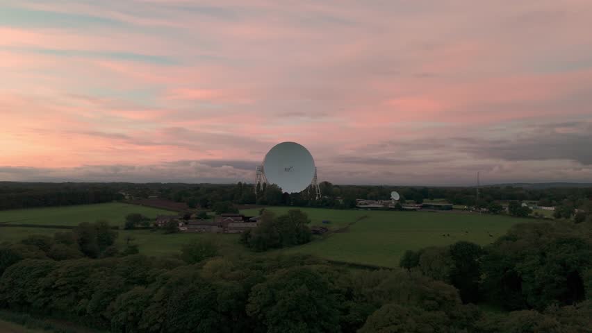 Large satellite dish at the Jodrell Bank Observatory under a pink sky