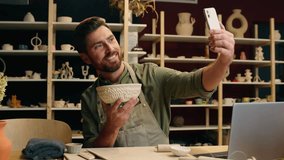 Happy smiling Caucasian man male guy small business owner potter entrepreneur blogger artist using mobile phone record video online blog social media showing pottery bowl photo selfie indoor workshop - Powered by Shutterstock - Get 15% off with code: PIKWIZARD15
