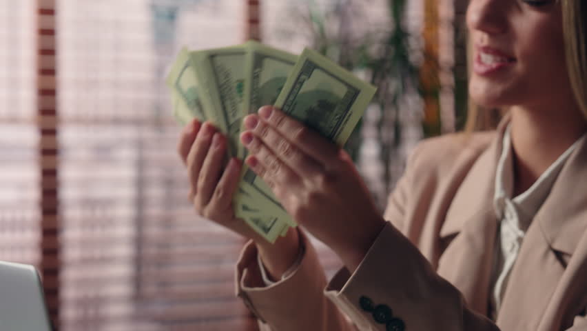 Happy pride rich smiling wealthy Caucasian girl freelancer business woman female entrepreneur boss businesswoman holding fan of money cash dollars wealth income salary winning prize finance in office