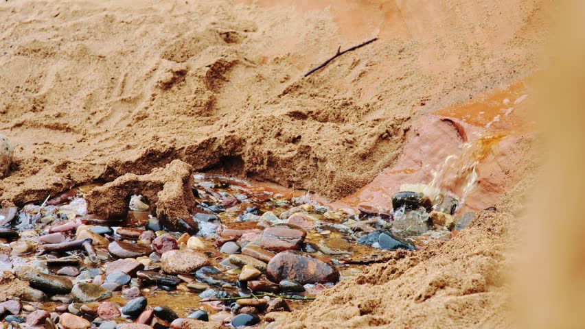 Small water stream carves a natural path through golden sand and pebbles - 4K