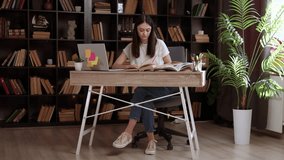 Smart female student using laptop to study in public library. Beautiful young woman learning online, preparing for exams, taking notes and writing an essay while sitting at an office table - Powered by Shutterstock - Get 15% off with code: PIKWIZARD15
