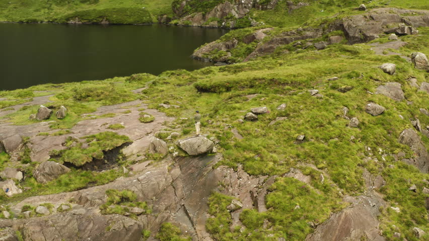 Man on rock formation during hike through hidden gem Lough Doon on the Dingle Peninsula, Conor Pass, Ireland.