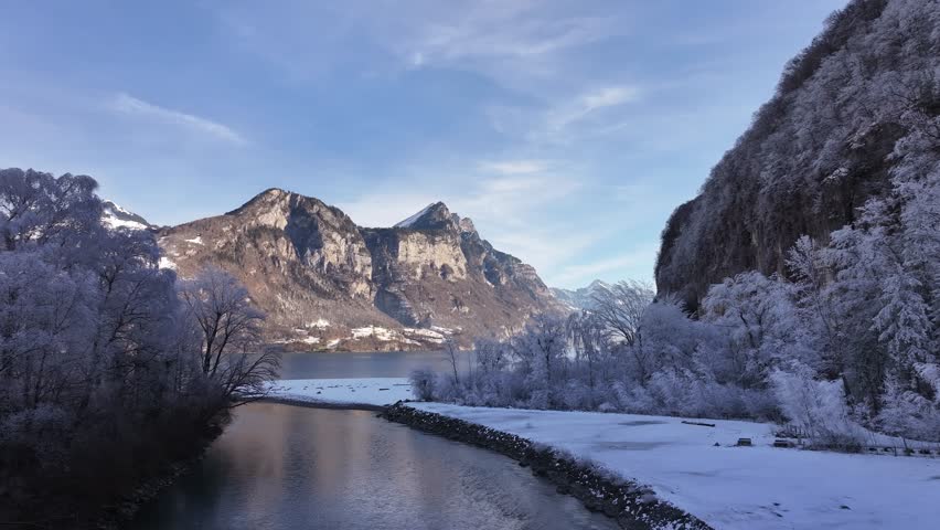 Snowy riverbank and frosted trees with mountains by Walensee in Switzerland