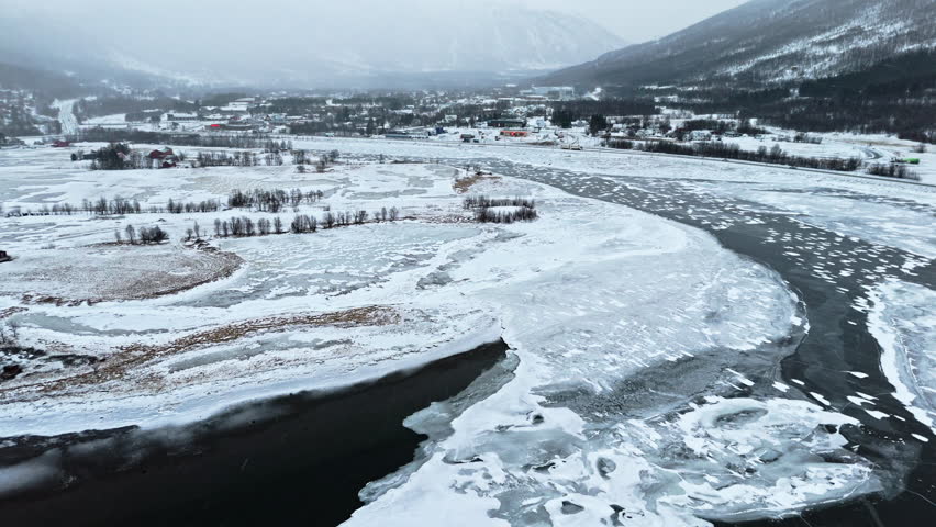 Frozen Tromsø fjords with icy river, snowy landscape, and distant mountains in winter