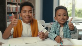 Happy little boys African American kids students pupils schoolboys friends siblings smiling children thumbs up gesture school primary education studying together writing desk classroom books learning - Powered by Shutterstock - Get 15% off with code: PIKWIZARD15