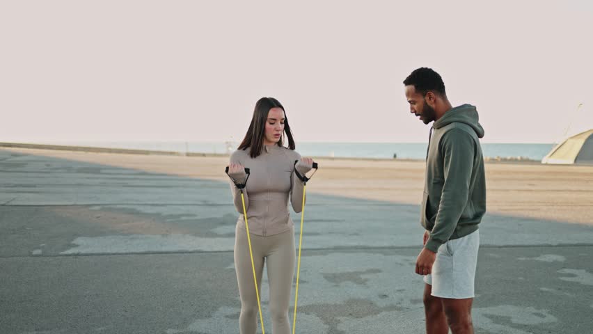 Personal trainer guiding woman in resistance band bicep curls