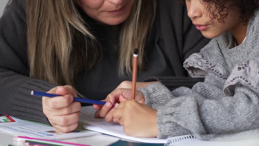 Caucasian mother and African American daughter studying at home, doing homework in cosy white room. Parent teach, child school girl learn knowledge, write exercise read book. Education for children